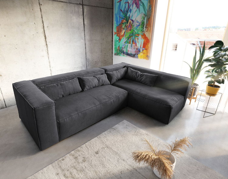 Wunderschöne Couch im Farbton Graphite mit variabler Ottomane vor Betonwand - Farbenfrohe Kunstwerke schaffen dazu einen tollen Kontrast